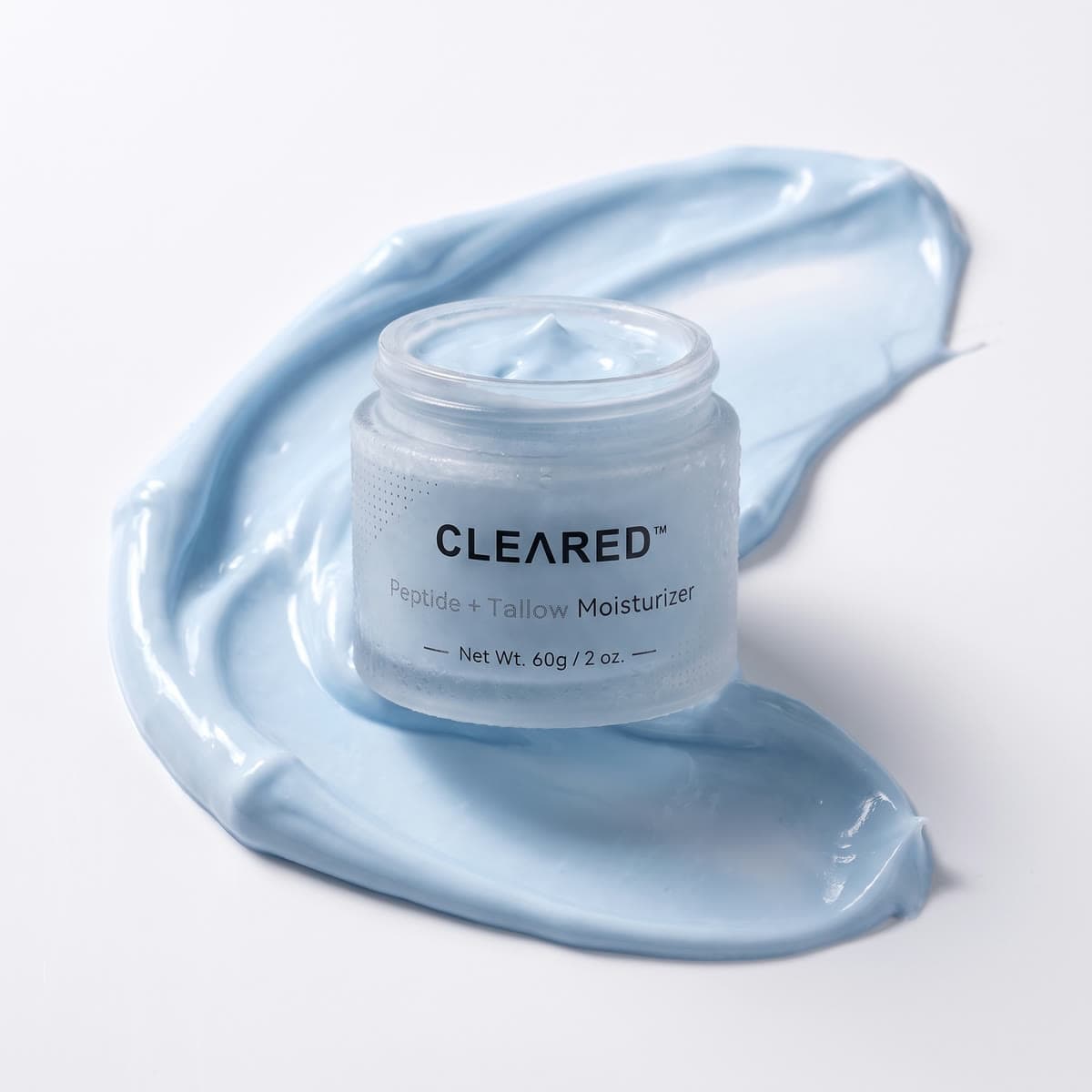 A jar of CLEARED Peptide + Tallow Moisturizer on a swipe of blue cream